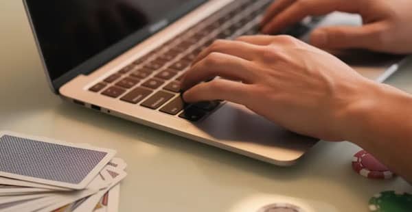 The image shows a pair of hands typing on a laptop keyboard, surrounded by playing cards and casino chips, suggesting an engaging online gambling experience. This scene captures the excitement of playing casino games and exploring deposit bonus offers in the world of online casinos.